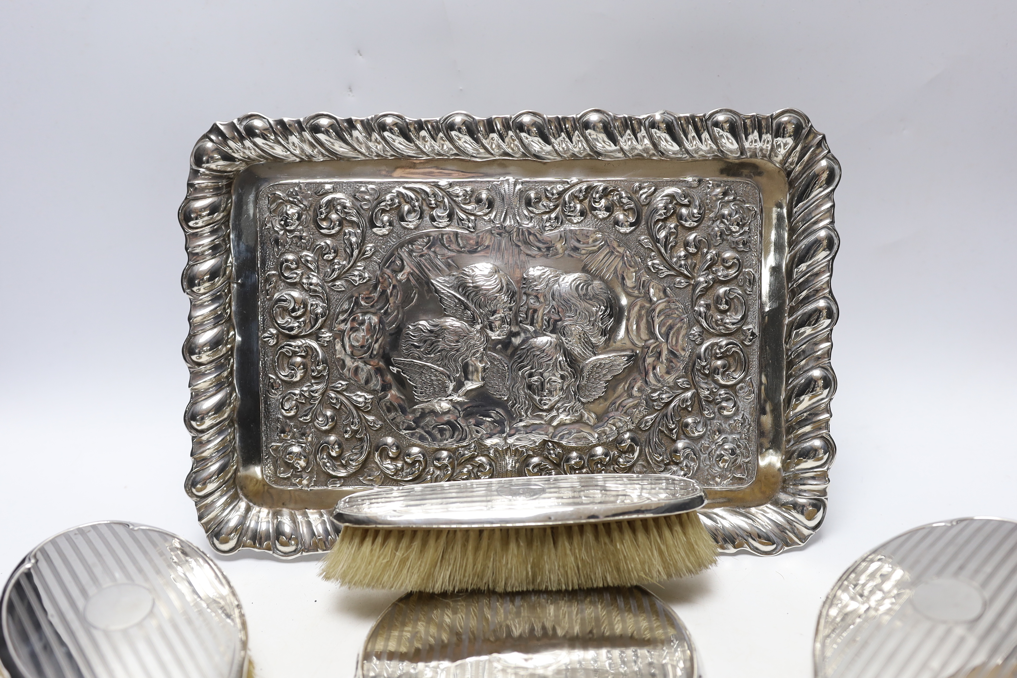 An Edwardian repousse silver dressing table tray, with Reynold's Angels decoration, Birmingham, 1904, 29.7cm, a silver dressing table mirror, two brushes, a clothes brush and two napkin rings.